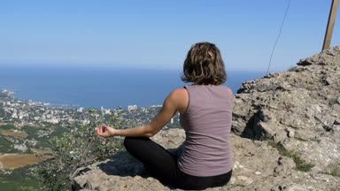 Kadın lotus pratik yoga konumda oturan taşır. Haç ile Cliff üst.