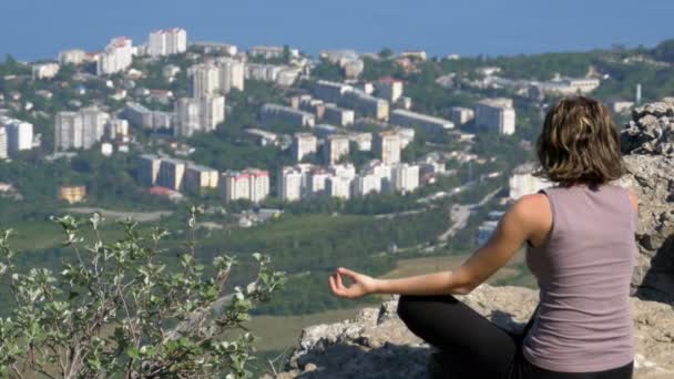 Femme assise en position lotus pratiquant des mouvements de yoga. Cliff top avec la croix . — Video