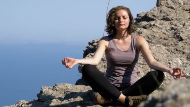 Mooie jonge vrouw beoefenen van Yoga en posities buiten op een ongelooflijke klif top instelling. — Stockvideo