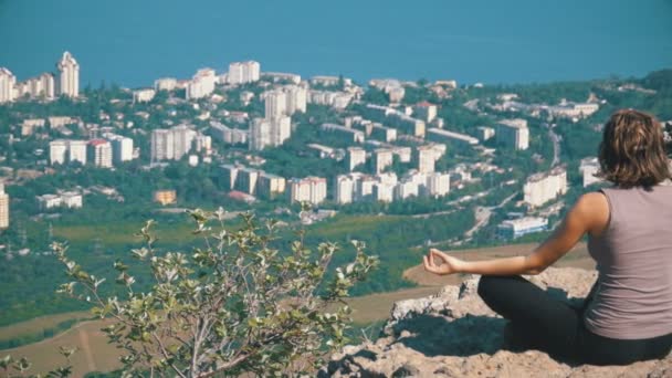 Sittande kvinna i lotusställning öva yoga flyttar. Bergstopp med korset. — Stockvideo