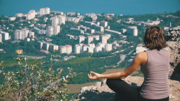 Sitting woman in lotus position practicing yoga moves. Cliff top with the cross. — Stock Video