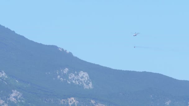 Vrtulník s vodní nádrž letí nad hory hasit požár. — Stock video