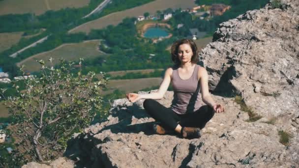 Dağlarda, lotus pozisyonunda bir uçurumun tepesinde oturan kadın yolcunun derin derin düşünür — Stok video