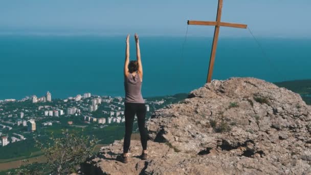 Una mujer practicando movimientos de yoga. Cliff top con la cruz . — Vídeos de Stock