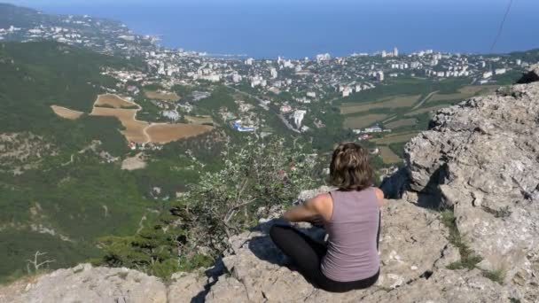 Mujer sentada en posición de loto practicando yoga se mueve o medita y levanta los brazos en las montañas . — Vídeos de Stock