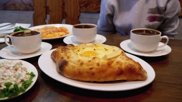 Adjarian khachapuri auf einem Tisch in einem georgischen Restaurant neben Salat, Omelette und Kaffee — Stockvideo