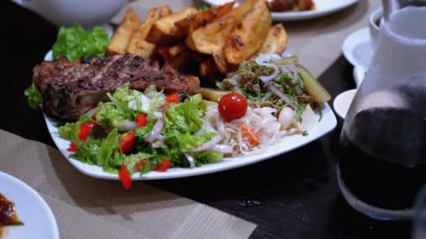 Steak auf Rippen mit Kartoffeln und Salat auf einem Tisch in einem georgischen Restaurant — Stockvideo