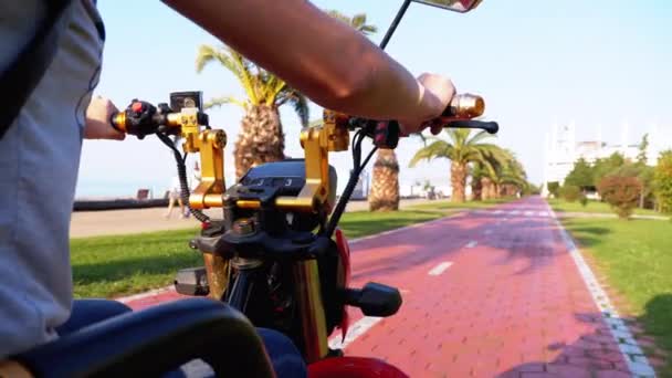 리조트 마을에 야자나무가 있는 빨간 자전거 길을 달리는 전기 스쿠터를 타는 여성 — 비디오