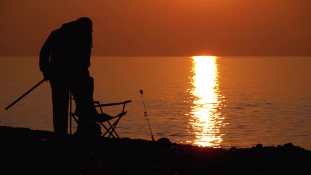 Silueta de un pescador al atardecer junto al mar. Silla de pesca, Caña de pescar, al atardecer . — Vídeo de stock