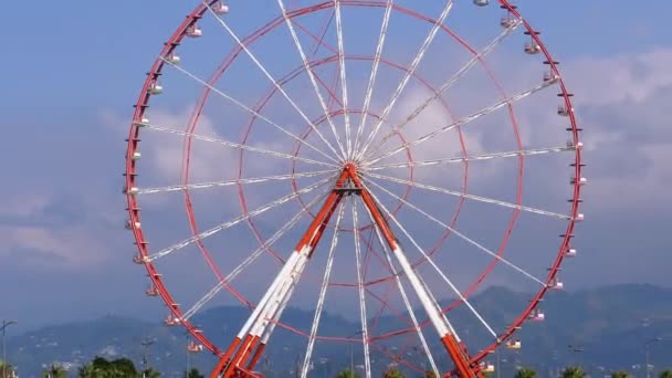 Колесо Ферріса проти блакитного неба з хмарами поблизу пальм у місті переселення, сонячний день. — стокове відео