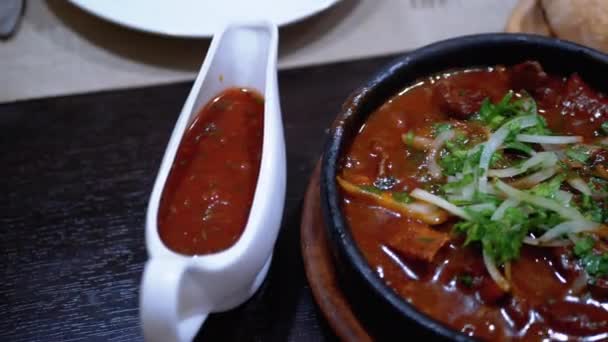 Georgian Meat Dish na Ketsi v restauraci. Chashushuli. Horké maso v hliněné pánvi na stole — Stock video