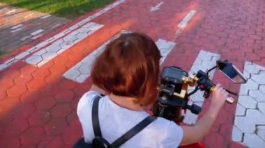 Kadın, tatil köyünde Palmiye ağaçlarıyla Kırmızı Bisiklet Yolunda Elektrikli Scooter sürüyor.