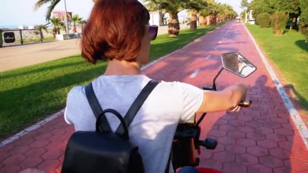 Vrouw rijdt een elektrische fiets op een rode fiets pad met palmbomen in het resort stad — Stockvideo