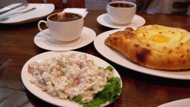 Аджария Хачапури на столе в грузинском ресторане рядом с салатом, омлетом и кофе — стоковое видео