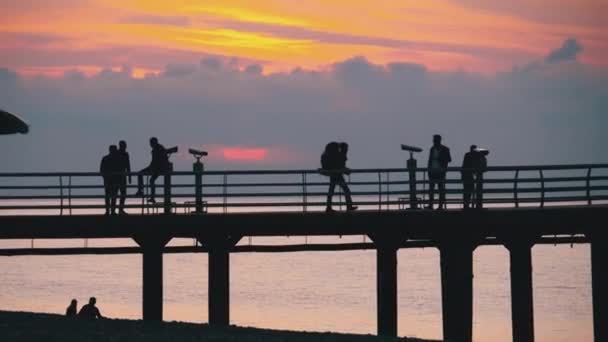 Siluetas de la gente en el muelle del mar durante la puesta del sol — Vídeo de stock
