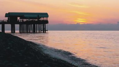 Gün batımının panorama 'sı Deniz' in üzerinde, iskelenin siluetinin yanında..