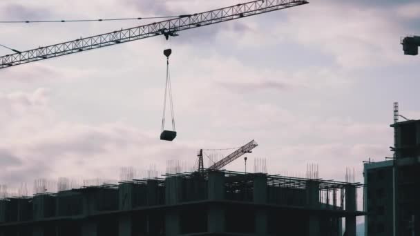 La grúa torre en un sitio de construcción eleva una carga en un edificio de gran altura . — Vídeos de Stock