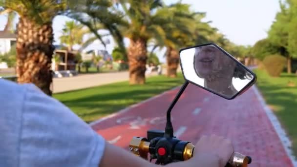 Femme fait du vélo électrique sur une piste cyclable rouge avec des palmiers dans la ville de villégiature — Video