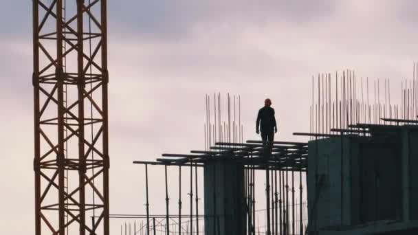 Silueta de un constructor al borde de un rascacielos en construcción. Trabajadores en una obra de construcción . — Vídeos de Stock