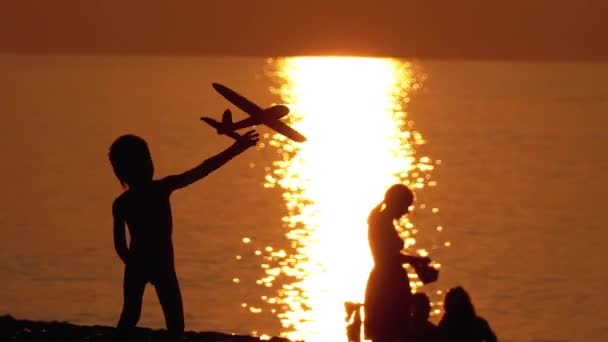 Silhouette di un bambino felice al tramonto in riva al mare Giocare con un aeroplano giocattolo. Famiglia felice . — Video Stock