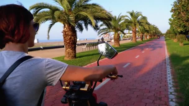 Frau fährt mit Elektrofahrrad auf rotem Radweg mit Palmen in der Kurstadt — Stockvideo