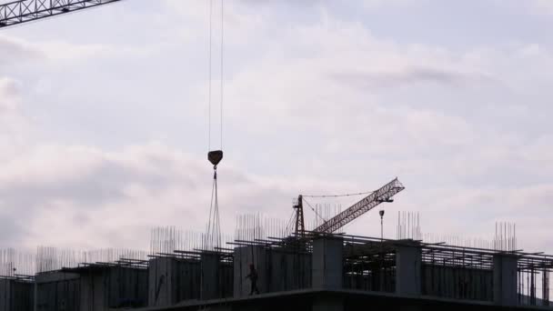 Torenkraan op een bouwplaats tilt een last op bij hoogbouw. — Stockvideo