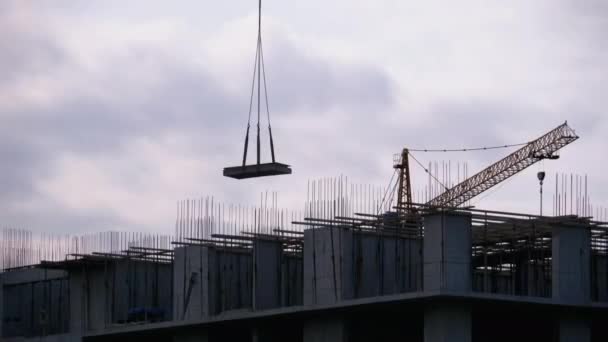 La grúa torre en un sitio de construcción eleva una carga en un edificio de gran altura . — Vídeo de stock