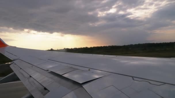 Vista desde la ventana de un avión de pasajeros en el ala durante el despegue al atardecer — Vídeo de stock