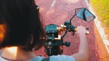 Kadın, tatil köyünde Palmiye ağaçlarıyla Kırmızı Bisiklet Yolunda Elektrikli Scooter sürüyor.