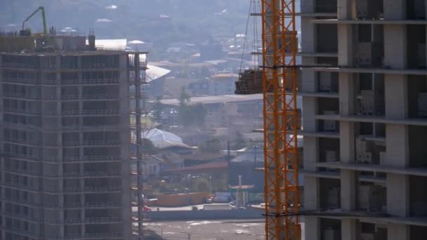 La grúa torre en un sitio de construcción eleva una carga en un edificio de gran altura . — Vídeos de Stock