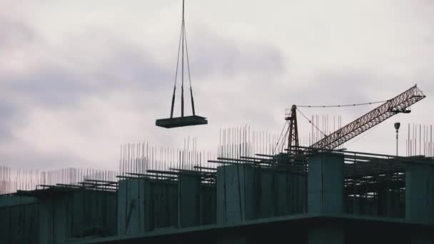 Une grue à tour sur un chantier soulève une charge dans un immeuble de grande hauteur . — Video