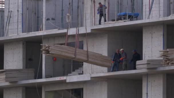 Construtores em um canteiro de obras. Guindaste em um canteiro de obras levanta uma carga. Construção de edifícios . — Vídeo de Stock