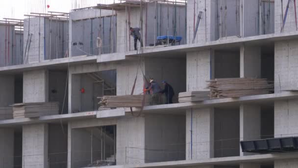 Arbetare på en byggarbetsplats. En kran på en byggarbetsplats lyfter en last. — Stockvideo