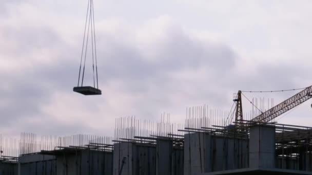 La grúa torre en un sitio de construcción eleva una carga en un edificio de gran altura . — Vídeos de Stock