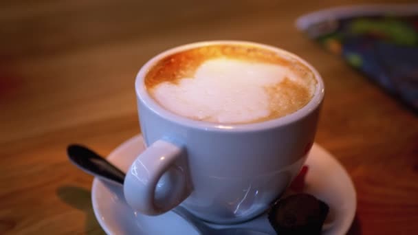 Restorandaki tahta masada beyaz köpüklü bir bardak Cappuccino. Yakın plan. — Stok video