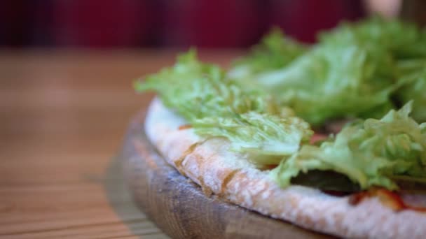 Pizza op een houten dienblad op een tafel in een restaurant Close-up. Gedetailleerde weergave van ingrediënten — Stockvideo