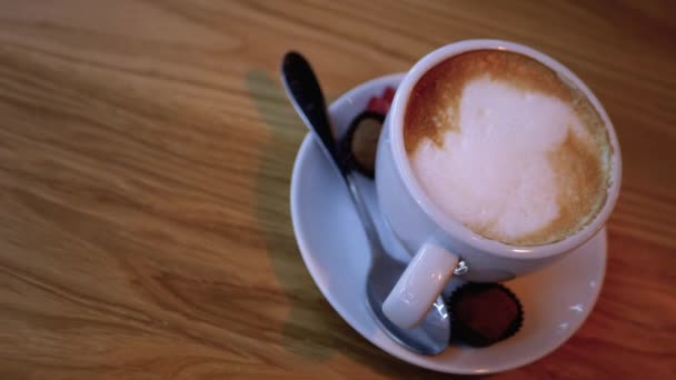 Filiżanka cappuccino z białą pianką na drewnianym stole w restauracji. Zbliżenie — Wideo stockowe
