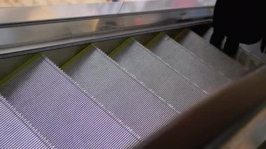 İnsanlar AVM 'de yürüyen merdivenden aşağı inip parmaklıkları tutuyorlar..