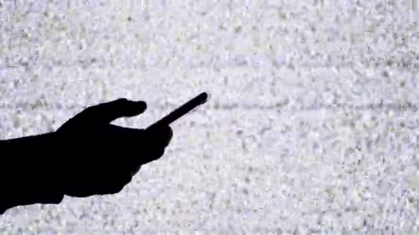 스마트폰 을 TV 화면에서 흰색 정적인 소음 과 함께 들고 있는 손의 실루엣 — 비디오