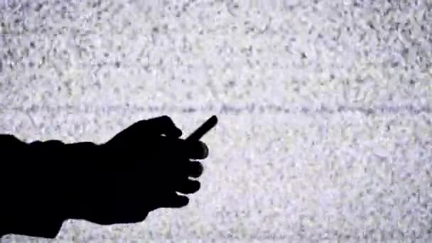 Silhouette of a Hand Holding a Smartphone on TV Screen Background with White Static Noise — Stockvideo