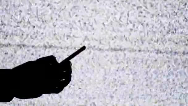 Silhouette d'une main tenant un smartphone sur fond d'écran de télévision avec bruit statique blanc 