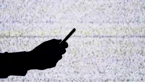 Silhouette d'une main tenant un smartphone sur fond d'écran de télévision avec bruit statique blanc 