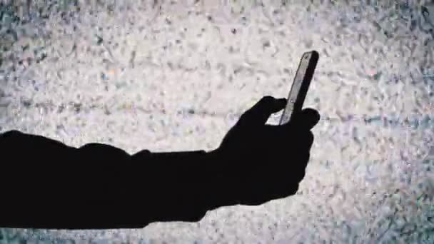 Silhouette einer Hand, die ein Smartphone auf dem Fernsehbildschirm hält, Hintergrund mit weißem statischen Rauschen — Stockvideo