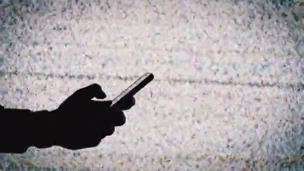 Silhouette of a Hand Holding a Smartphone on TV Screen Background with White Static Noise — Stockvideo