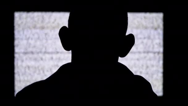 La silhouette di una testa anonima dei fan sta guardando il rumore statico bianco e l'interferenza della TV — Video Stock