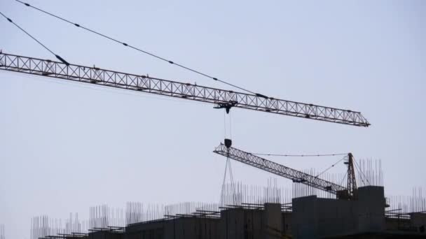 Torenkraan op een bouwplaats tilt een last op bij hoogbouw. — Stockvideo