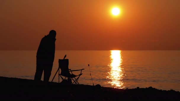 Silhueta de um pescador ao pôr-do-sol junto ao mar. Cadeira de pesca, Rod de pesca, no caminho do pôr do sol . — Vídeo de Stock