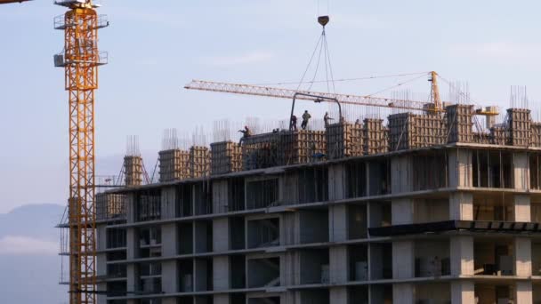 Construcción de edificios. Una grúa en un sitio de construcción levanta una carga. Trabajadores en una obra de construcción — Vídeo de stock