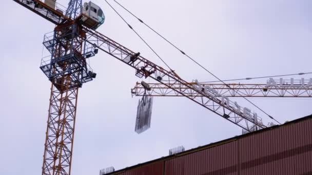 Construção de edifícios. Um guindaste em um canteiro de obras levanta uma carga . — Vídeo de Stock