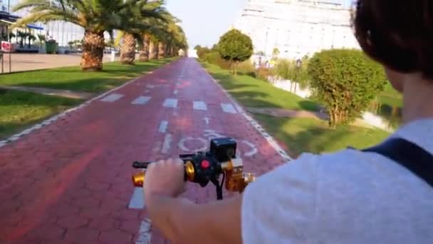 Mujer monta una vespa eléctrica en un carril bici rojo con palmeras en la ciudad del Resort — Vídeo de stock